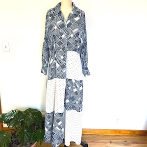 May include: A long-sleeved maxi dress featuring a patchwork design of dark blue and white geometric patterns alternating with white fabric panels covered in small black polka dots, a collared neckline, and a button-down front closure.