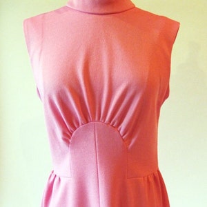 May include: A sleeveless pink dress with a high neckline and a fitted bodice. The bodice has a unique design with a curved seam that creates a sunburst effect.