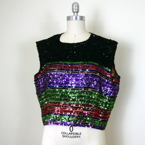 Może przedstawiać: Bezrękawnik z cekinami, z czarnym gorsetem i wielokolorowym paskowanym dołem. Paski są zielone, czerwone, fioletowe i niebieskie.