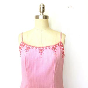 May include: A light pink dress with thin straps and a square neckline. The neckline and straps are embellished with pink and white beads and sequins. The dress is displayed on a mannequin.