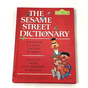 May include: A red hardback book titled The Sesame Street Dictionary, featuring illustrations of Bert and Ernie on the front cover. The text includes A first book of words and their meanings, Over 1,300 entries, each illustrated in full colour.
