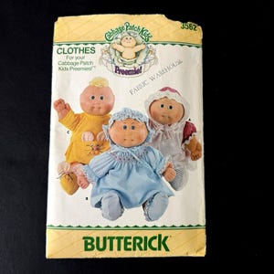 Könnte beinhalten: Ein Vintage-Butterick-Schnittmuster für Cabbage Patch Kids Preemie-Puppenkleidung. Das Muster zeigt Illustrationen von drei Puppen in verschiedenen Outfits. Die Verpackung ist gelb und grün mit dem Text "CLOTHES" und "BUTTERICK".