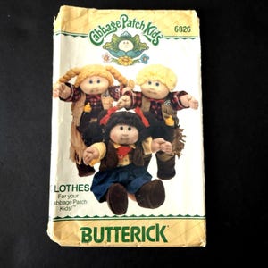 Könnte beinhalten: Vintage Cabbage Patch Kids Schnittmuster. Das Muster zeigt drei Puppen in Cowboy-Outfits. Auf dem Cover des Musters steht der Text "LOTHEs For your Cabbage Patch Kids!" und das Butterick-Logo.