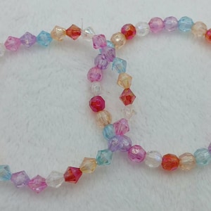 May include: Two beaded bracelets. One bracelet features faceted, multi-coloured beads in shades of pink, orange, blue, and clear. The other bracelet has round, multi-coloured beads. Both bracelets are on a white surface.