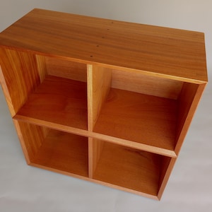 May include: A wooden storage cube with four open compartments. The cube is constructed from light brown wood with visible grain, and the edges are neatly joined. The design is simple and functional, suitable for various storage needs.