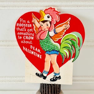 May include: Vintage Valentine's Day card featuring a child in a rooster costume. The red heart-shaped card has the text "I'm a rooster that's got something to crow about DEAR VALENTINE." The child is wearing a green vest, blue shorts, and black shoes.
