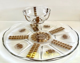 May include: A clear glass serving dish with a gold leaf design. The dish has a central bowl and a divided tray with a scalloped edge. The gold leaf design includes a crown and leaf pattern.