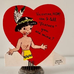 May include: Vintage Valentine's Day card in the shape of a red heart. The card features a cartoon Native American boy with a feather headdress and the text "Valentine, how can I tell 'Feather' you are mine?"