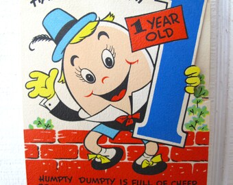 May include: Vintage birthday card featuring Humpty Dumpty holding a large blue number one. The card reads "Happy Birthday" and "1 Year Old." The bottom of the card has the text "Humpty Dumpty is full of cheer because your very first birthday is here."