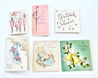 May include: A collection of vintage greeting cards with various designs. Cards include text such as "For Your Bridal Shower," "A Gift for Your Shower," and "A Wedding Gift." The cards feature illustrations of umbrellas, bells, and a baby.