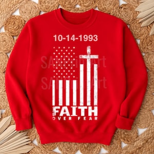 May include: A red sweatshirt with a white graphic of the American flag, a cross, and the text "FAITH OVER FEAR." The date "10-14-1993" is printed above the flag. The sweatshirt has a crew neck and long sleeves.