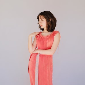 Könnte beinhalten: Eine Frau trägt ein korallenfarbenes Maxikleid mit einem hellblauen Gürtel. Das Kleid hat ein plissiertes Design und einen Rüschen-Saum.