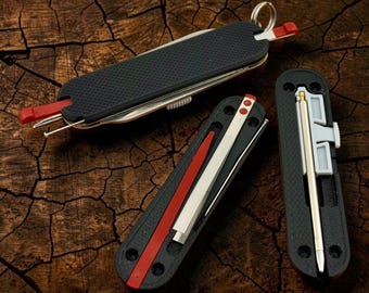 May include: A black multi-tool pocket knife with a textured grip, featuring a metal key ring, a red plastic toothpick, and a silver metal pin. Two additional black handle scales are shown, one containing a red plastic tool and one with a pen.