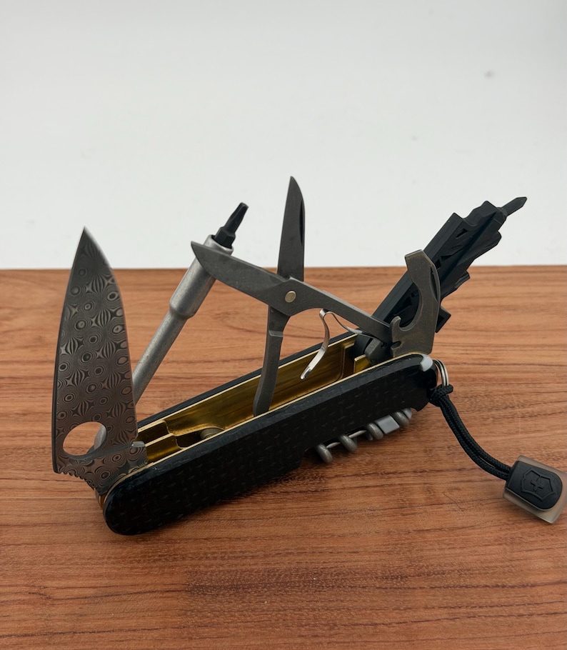 May include: A multi-tool pocket knife with a black textured handle and gold-colored interior. It features a Damascus steel blade with a circular cutout, a metal bit driver, scissors, a bottle opener, and a black lanyard with a small logo tag.