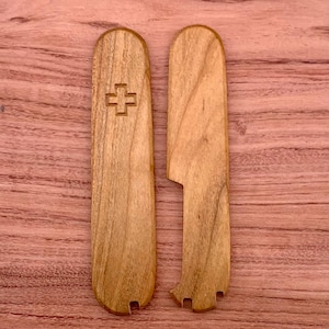 Puede incluir: Dos cachas de navaja de bolsillo de madera. Una cacha presenta un diseño de cruz tallada. Las cachas son de madera marrón claro y tienen un acabado liso. Las cachas están diseñadas para adaptarse a una navaja de bolsillo.