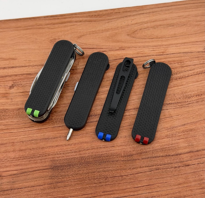 May include: A collection of black pocket knives with textured grips. One multi-tool knife has green and white accents. Other knives have blue and red accents. All knives are on a wooden surface.