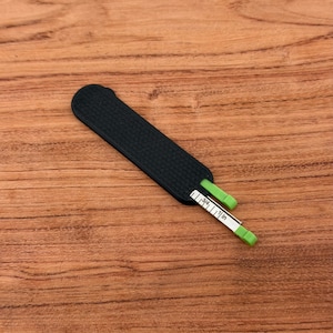 May include: A black, rectangular measuring tool with a textured surface. A white and green measuring tape is partially extended, displaying inch measurements. The tool is designed for measuring small objects.