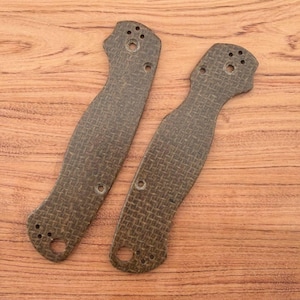 May include: Two textured, dark brown knife handle scales with multiple holes for attachment. The scales have a curved shape and a woven pattern, set against a wooden background.