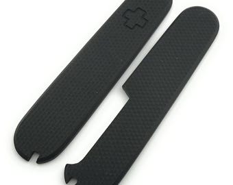 May include: Two black replacement scales for a pocket knife. One scale has a textured surface and a recessed cross symbol. The other scale has a textured surface and a notch at the end.