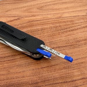 May include: A black multi-tool with a textured grip and a built-in ruler. The ruler is silver with blue accents and measures in inches. The tool is partially open, revealing other implements.