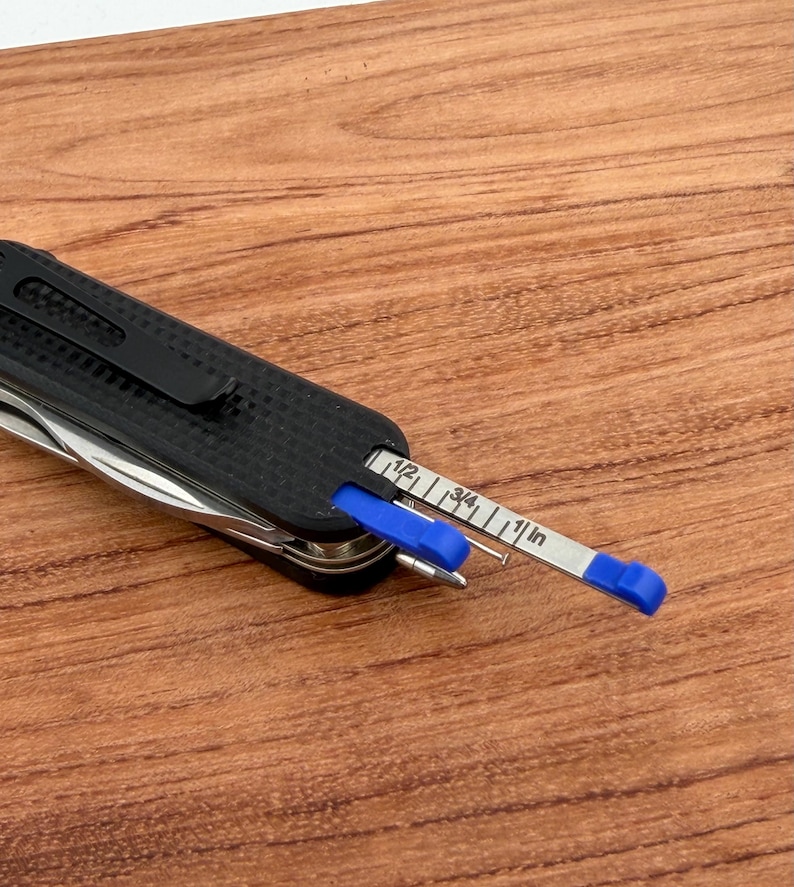 May include: A black multi-tool with a textured grip and a built-in ruler. The ruler is silver with blue accents and measures in inches. The tool is partially open, revealing other implements.