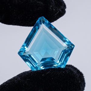 May include: A kite-shaped, faceted blue gemstone with a brilliant cut and high clarity. The stone exhibits a vibrant, translucent sky-blue colour with sharp, geometric edges and symmetrical facets that reflect light across its polished surface.