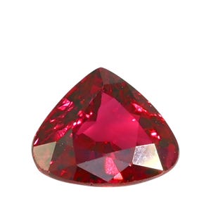 Op de afbeelding: Een gefacetteerde, hartvormige robijn edelsteen. De edelsteen heeft een diepe, verzadigde rode kleur met meerdere facetten die licht reflecteren. De vorm is een afgeronde driehoek, met een gepolijst oppervlak.