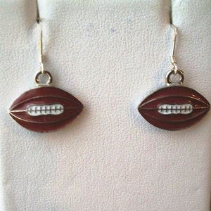 May include: A pair of silver earrings with a red and white football charm. The football is a traditional American football shape.
