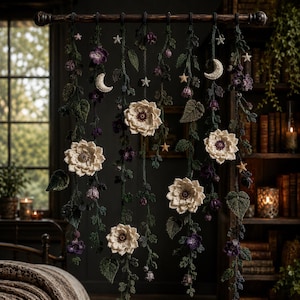 May include: A wall hanging featuring multiple crocheted vines suspended from a dark wooden rod. The vines are adorned with cream-coloured flowers, dark purple blossoms, green leaves, small white stars, and crescent moons made of yarn.