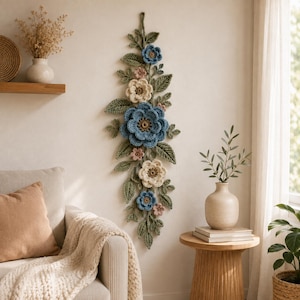 Peut inclure: Une d&eacute;coration murale verticale compos&eacute;e de fleurs et de feuilles au crochet dans des tons bleu, cr&egrave;me et rose poudr&eacute;, agr&eacute;ment&eacute;e d'un feuillage vert sauge. L'ensemble pr&eacute;sente plusieurs fleurs superpos&eacute;es et des feuilles textur&eacute;es dispos&eacute;es en une longue cascade botanique.