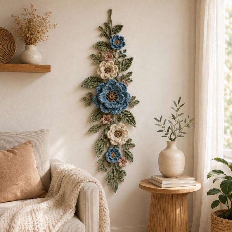 Peut inclure: Une d&eacute;coration murale verticale compos&eacute;e de fleurs et de feuilles au crochet dans des tons bleu, cr&egrave;me et rose poudr&eacute;, agr&eacute;ment&eacute;e d'un feuillage vert sauge. L'ensemble pr&eacute;sente plusieurs fleurs superpos&eacute;es et des feuilles textur&eacute;es dispos&eacute;es en une longue cascade botanique.