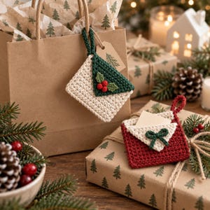 May include: Two crocheted envelope ornaments. One is cream with a dark green flap featuring red holly berries and green leaves. The other is red with a cream flap featuring a dark green bow. Both have loops for hanging and small paper inserts.