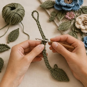 Peut inclure: Un crochet en m&eacute;tal avec un manche en bois est utilis&eacute; avec du fil vert olive pour cr&eacute;er une longue bande &eacute;troite avec une boucle &agrave; une extr&eacute;mit&eacute; et une pi&egrave;ce en forme de feuille &agrave; l'autre, entour&eacute;e d'autres feuilles et fleurs au crochet.