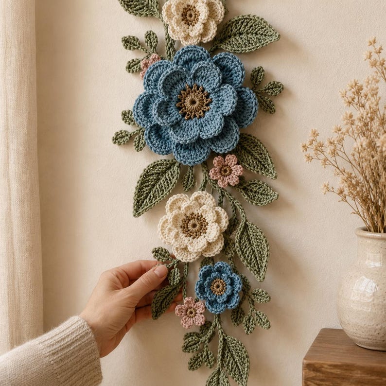 Peut inclure: Une d&eacute;coration murale verticale compos&eacute;e de fleurs au crochet dans des tons bleu, cr&egrave;me et rose p&acirc;le, agr&eacute;ment&eacute;e de feuilles et de tiges crochet&eacute;es vertes. L'ensemble comprend plusieurs fleurs superpos&eacute;es avec des c&oelig;urs textur&eacute;s.