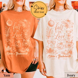 May include: Two short-sleeve t-shirts, one in burnt orange and one in ivory, each featuring a graphic print with the text 'fall in Love est. 2026' and 'Olivia's Bachelorette', alongside illustrations of a disco ball, wine glasses, rings, and a bottle.