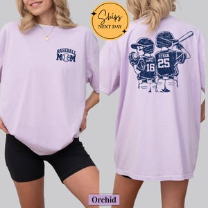 May include: Orchid-colored t-shirt with "Baseball Mom" text on the front and a baseball player graphic on the back. The graphic includes the names "Daniel" and "Ethan" with the numbers 16 and 25. The shirt has a relaxed fit.