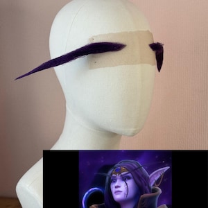 Puede incluir: Una cabeza de maniquí con orejas de elfo cosplay moradas sujetas con cinta adhesiva. Las orejas son largas y puntiagudas. Una ilustración digital de un personaje elfo de la noche está en la esquina inferior derecha.