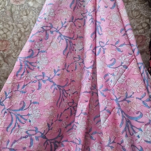 May include: Pink floral fabric with a repeating pattern of white and light pink flowers, blue vines, and leaves. The fabric is folded, showing the pattern's intricate details. The overall theme is floral and textile.