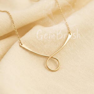 May include: A gold-toned necklace featuring a delicate chain and a central pendant formed by a curved metal bar that loops into a circular shape at the bottom. The design is symmetrical with a smooth, polished finish and a thin, refined metal link chain.