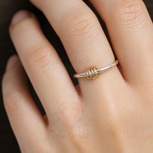 May include: A silver ring with three gold-colored interlocking circles as a focal point. The ring is on a finger, showcasing the contrast between the silver band and the gold accents. The design is simple yet elegant.