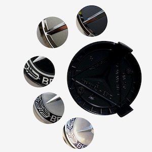 May include: A black Mercedes-Benz wheel center cap with silver accents. The cap features the Mercedes-Benz logo, a three-pointed star within a circle, and the letters "B" and other text. Several close-up details of the logo are shown.