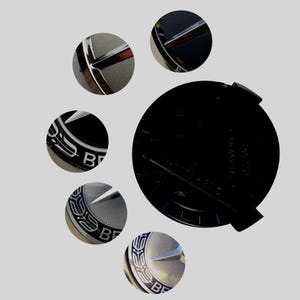 Könnte beinhalten: Eine kreisförmige schwarze Kunststoff-Emblemkappe für Fahrzeuge mit einem silbernen dreizackigen Stern-Logo. Das Design umfasst einen strukturierten silbernen Hintergrund mit einem blauen Rand und dem Schriftzug "BRABUS" in silbernen Buchstaben.