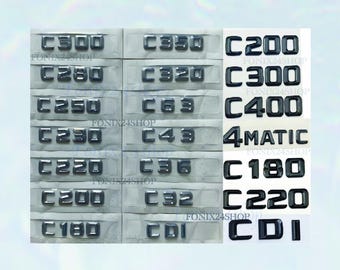 May include: A collection of black car emblems, including C300, C350, C200, C280, C320, C300, C250, C63, C400, C230, C43, 4MATIC, C220, C36, C180, C32, C220, and CDI. The emblems are displayed on a light gray background.