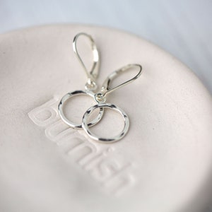 May include: A pair of silver dangle earrings with hammered circle pendants. The earrings have a simple, minimalist design.
