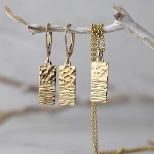 May include: Gold-toned jewelry set featuring a necklace and matching earrings. The rectangular pendants have a textured upper half and a linear lower half. The earrings have lever-back closures, and the necklace has a delicate chain.