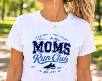 May include: A white short-sleeved crop top featuring a blue graphic print that reads MOMS RUN CLUB in bold lettering, with the text STRONG MOMS STRONGER TOGETHER and ONE MILE AT A TIME, plus a small illustration of a running shoe centered below.