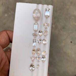 Puede incluir: Una colección de gemas talladas en tonos claros, melocotón y champán. Las gemas, de formas ovaladas, rectangulares y de pera, se exhiben sobre una superficie blanca. Las gemas son de varios tamaños.