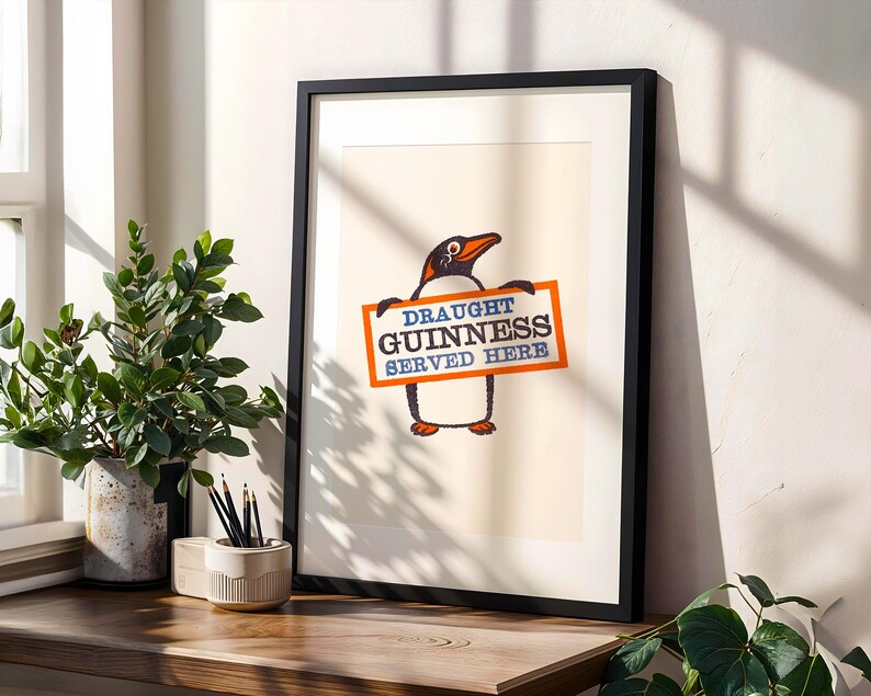 May include: Framed print of a penguin holding a sign saying "Draught Guinness Served Here." The penguin is black and white with an orange beak and feet. The sign is orange with blue and white text. The print is in a black frame, suitable for a pub or home bar.