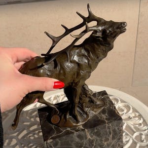 May include: A bronze sculpture of a stag in a dynamic pose, mounted on a marble base. The stag is depicted with detailed antlers and a textured surface, showcasing the artist's skill. The sculpture is approximately 12 inches tall.