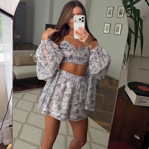 May include: A two-piece set consisting of a cropped camisole top and matching high-waisted shorts, both featuring a sheer, lightweight fabric with a grey and blue abstract floral print. The top has thin straps, and the shorts have an elastic waistband.